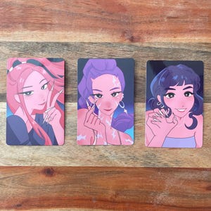 May include: Three rectangular art prints featuring stylized illustrations of women with long nails. The first has pink hair and is making a peace sign. The second has purple hair and is making a heart shape. The third has dark blue hair and is smiling.