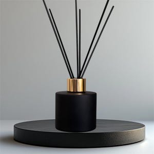 Könnte beinhalten: Ein schwarzer Aromatherapie-Diffusor mit goldfarbenem Kragen und schwarzen Stäbchen. Die zylindrische Flasche steht auf einer dunkelgrauen, runden Plattform. Die Stäbchen erstrecken sich nach oben und schaffen ein minimalistisches und elegantes Design.
