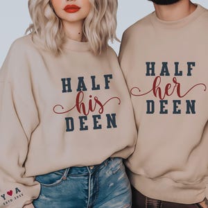 May include: Beige sweatshirts with the text "HALF his DEEN" and "HALF her DEEN" in navy blue block letters with a red cursive "his" and "her". The sleeves have a small heart and the letters "Y♥A ESTD 2023".