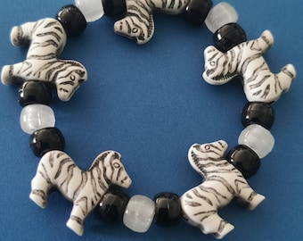 May include: A black and white zebra bead bracelet with alternating black and white beads. The bracelet is made of plastic and has a stretchy band.