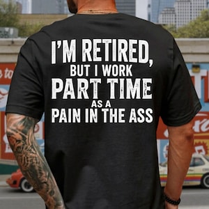 Może przedstawiać: Czarny t-shirt z krótkim rękawem z białym napisem w stylu vintage na plecach: I'M RETIRED, BUT I WORK PART TIME AS A PAIN IN THE ASS. Koszulka ma okrągły dekolt i jest wykonana z jednolitego czarnego materiału z wyraźnymi, pogrubionymi literami.