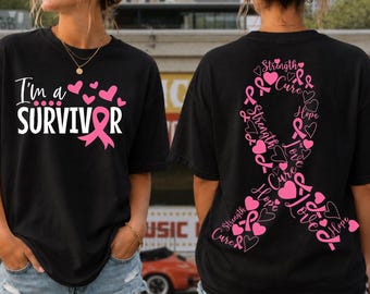 May include: A black t-shirt featuring a pink ribbon graphic and the text I'm a SURVIVOR on the front. The back displays a large pink ribbon composed of the words Strength, Cure, Hope, and Love, interspersed with small pink heart illustrations.