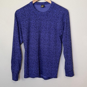 May include: A long-sleeve crew neck shirt featuring a horizontal striped pattern in shades of dark blue and black. The garment has a ribbed collar and cuffs, with a small rectangular brand label visible on the inside of the neckline.
