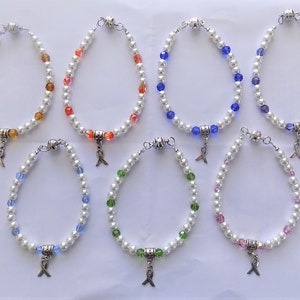 May include: Eight pearl bracelets with different colored beads and a silver charm in the shape of a ribbon. The bracelets are arranged in two rows of four.