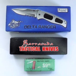 May include: Three boxes for tactical knives. The top box is blue with a silver knife and the text "DELTA RANGER". The middle box is black with the text "Barracuda Tactical Knives". The bottom box is green with the text "MILITARY KNIFE", "$9.95", "5 Function", and "Flying Falcon".