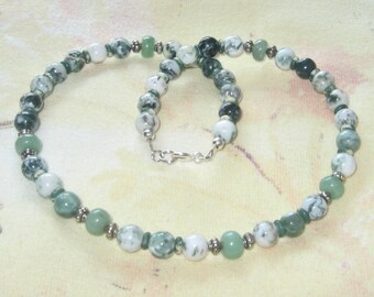 May include: A beaded necklace featuring a variety of green and white stones. The necklace has a silver clasp and is composed of round and oval beads. The beads are a mix of solid green, speckled white and green, and solid white.