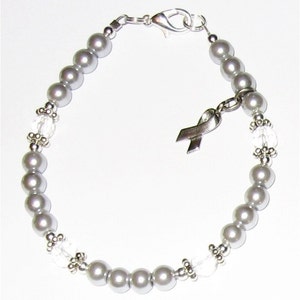 May include: A silver bracelet with gray pearls and clear crystal beads. A silver ribbon charm hangs from the bracelet.