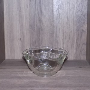 May include: A clear glass bowl with a scalloped edge. The bowl is empty and sitting on a wooden surface.