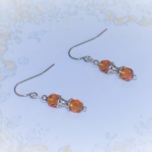 May include: A pair of silver earrings with amber-colored glass beads. The beads are faceted and have a slightly irregular shape.