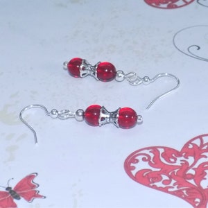 May include: A pair of silver dangle earrings with two red glass beads on each earring.
