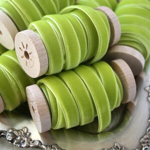 May include: Close-up of spools of green velvet ribbon. The ribbon is wound around wooden spools with a natural finish. The ribbon is a light shade of green, almost a lime green.