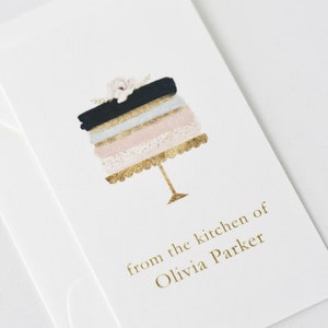 May include: A white card with a gold cake illustration and the text "from the kitchen of Olivia Parker".