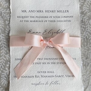 K&ouml;nnte beinhalten: Eine Hochzeitseinladung mit einem rosa Band darum gebunden. Die Einladung ist auf strukturiertem Papier gedruckt und lautet "MR. AND MRS. HENRY MILLER REQUEST THE PLEASURE OF YOUR COMPANY AT THE MARRIAGE OF THEIR DAUGHTER Emma Elizabeth Hexa TWO THOUSAND TW F PAST SIX IN THE EVENIN VE DOVER HALL 150 MANAKIN RD, MANAKIN-SABOT, VIRGIN reception to follow"