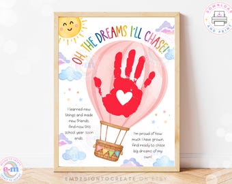 Puede incluir: Una impresión enmarcada con una huella de mano roja dentro de una ilustración de globo aerostático rosa. La impresión incluye el texto "OH, THE DREAMS I'LL CHASE!" y otro texto sobre el crecimiento y los sueños. También se representa un sol sonriente y nubes.