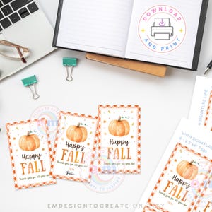 May include: A selection of autumn-themed gift tags and printables. The tags display a watercolour pumpkin, the words "Happy Fall", and a decorative border. A laptop, glasses, and stationery are also visible.