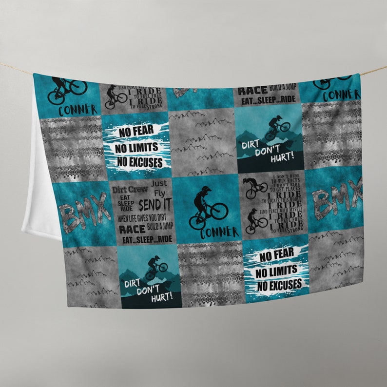 K&ouml;nnte beinhalten: Eine t&uuml;rkisfarbene und graue Patchwork-Decke mit BMX-Motiv. Die Decke zeigt verschiedene S&auml;tze wie "Ich fahre, um mich stark zu f&uuml;hlen", "Keine Angst, keine Grenzen, keine Ausreden", "Dreckschmutz tut nicht weh" und "Schick es". Die Decke ist mit dem Namen "Conner" personalisiert.
