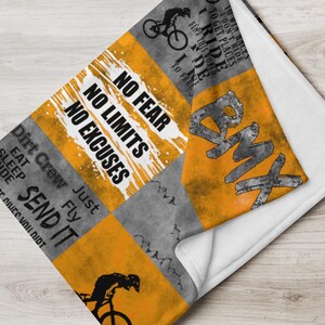 K&ouml;nnte beinhalten: Orange-graue gemusterte Fleece-Decke mit dem Text "No Fear, No Limits, No Excuses" und "Dirt Crew Just Fly Send It". Die Decke zeigt au&szlig;erdem eine BMX-Fahrradgrafik und das Wort "BMX" in gro&szlig;en Buchstaben.
