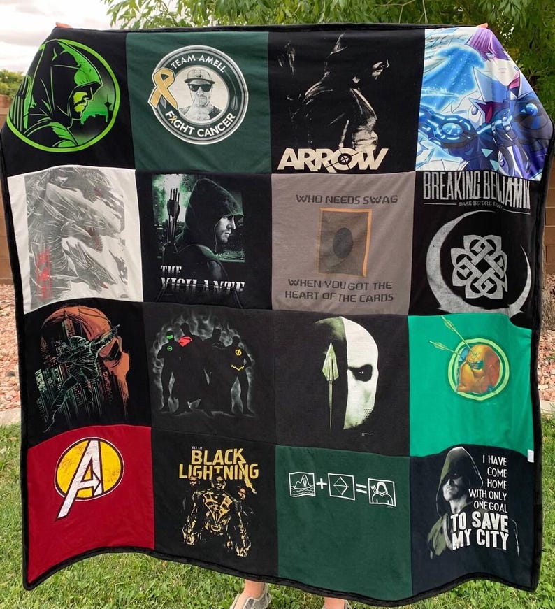 May include: A patchwork quilt constructed from various graphic t-shirts featuring superhero and pop culture themes. The quilt displays diverse prints including Arrow, Breaking Benjamin, Black Lightning, and Avengers logos, alongside text like "Who needs swag when you got the heart of the cards" and "I have come home with only one goal to save my city."