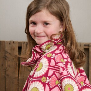 May include: A young girl wearing a pink and white patterned dress with a high collar. The dress has a floral design with pink, white, and green flowers.