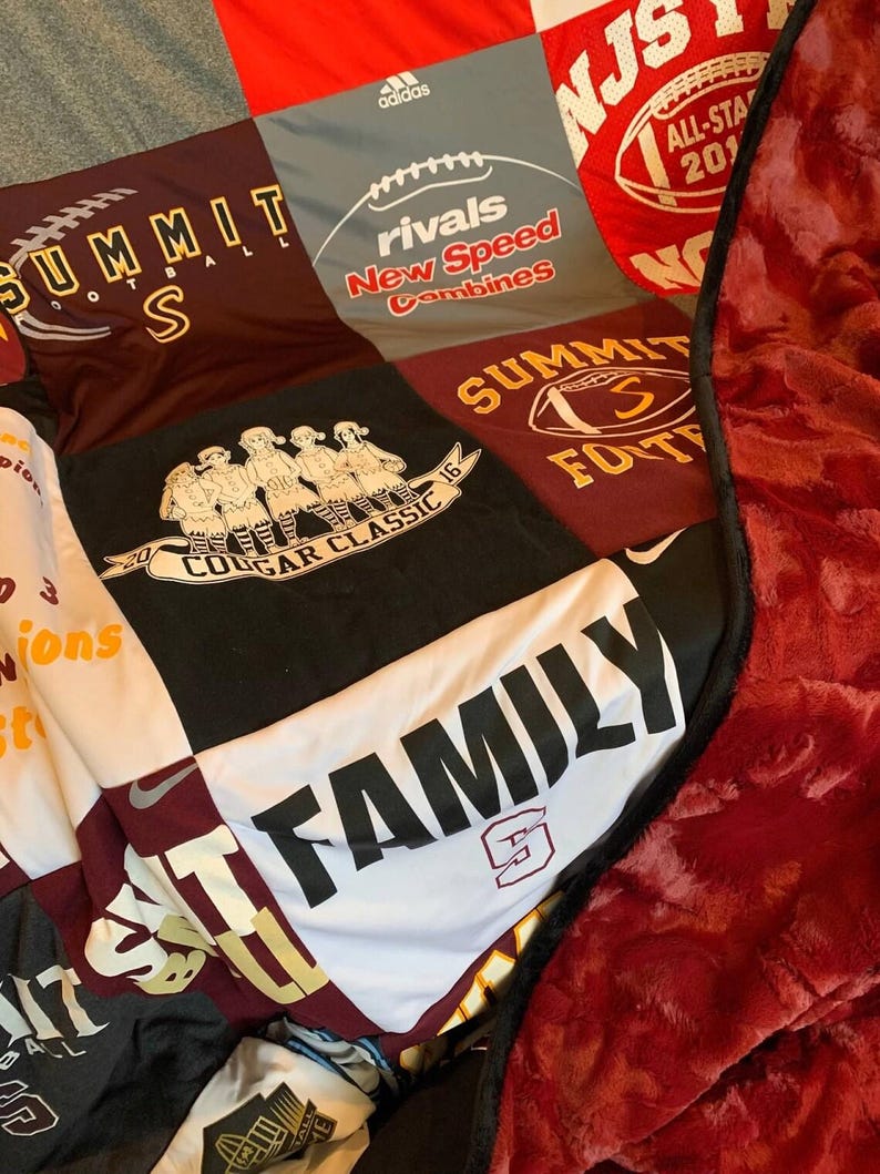 May include: A patchwork quilt made from various athletic t-shirts featuring logos and text including Summit Football, Rivals New Speed Combines, Cougar Classic 2016, and Family. The quilt has a deep red, textured plush backing with a black border.