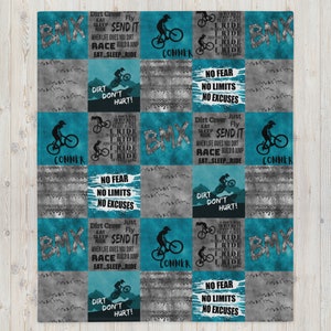 K&ouml;nnte beinhalten: Eine t&uuml;rkisblaue und graue Steppdecke mit BMX-Bike-Motiv. Die Steppdecke zeigt ein sich wiederholendes Muster aus BMX-Bikes, Dreck und motivierenden Zitaten. Die Zitate beinhalten "Dirt Don't Hurt!" und "No Fear, No Limits, No Excuses".