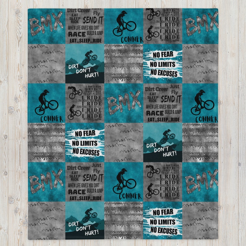 K&ouml;nnte beinhalten: Eine t&uuml;rkisblaue und graue Steppdecke mit BMX-Bike-Motiv. Die Steppdecke zeigt ein sich wiederholendes Muster aus BMX-Bikes, Dreck und motivierenden Zitaten. Die Zitate beinhalten "Dirt Don't Hurt!" und "No Fear, No Limits, No Excuses".