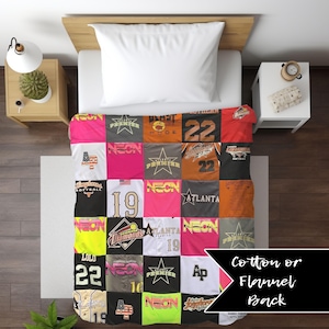 May include: A patchwork quilt made from repurposed t-shirts with various sports-themed designs and text, including "Longhorns Softball", "Diamonds", "Atlanta", "Neon", and "22". The quilt has a cotton or flannel back.