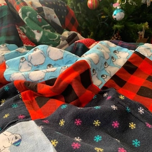 May include: A patchwork quilt featuring various fabric patterns including light blue panels with penguin illustrations, red and black buffalo plaid squares, and a dark navy blue fabric decorated with small, colorful embroidered snowflake motifs.