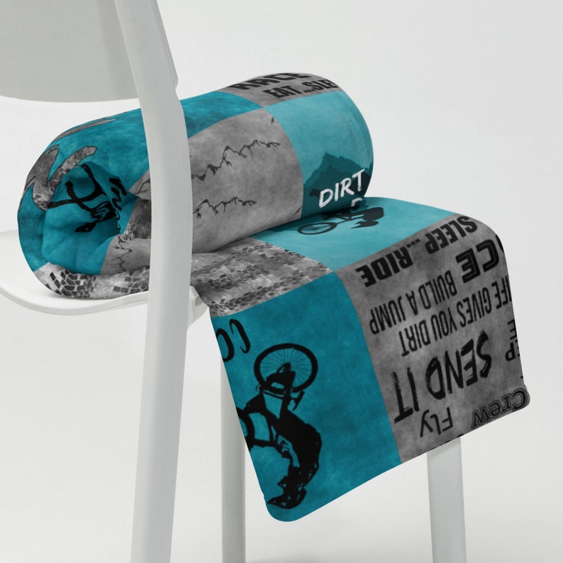 K&ouml;nnte beinhalten: Eine tealblaue und graue Fleece-Decke mit einem Mountainbike-Design und dem Text "Crew Fly Send It", "Dirt", "Sleep... Ride", "Afe Gives You Dirt", "Ce Build A Jump" und "Co".