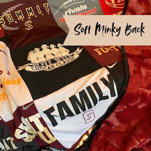 May include: A patchwork quilt made from various athletic t-shirts in maroon, black, and white, featuring printed text including Summit Football, Cougar Classic 2016, and Family. The quilt has a dark red textured minky fabric backing and black trim.