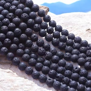 Peut inclure: Un brin de perles en roche volcanique noire. Les perles sont rondes et ont une texture rugueuse et poreuse.