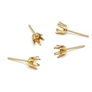 Peut inclure: Quatre montures de boucles d'oreilles dorées avec un design à griffes. Chaque monture a une tige pour l'insertion dans l'oreille. Les montures sont présentées sur un fond blanc.