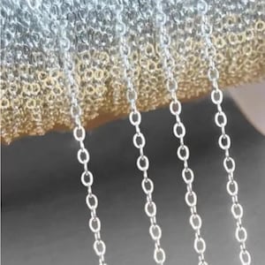 May include: A close-up of four silver chains hanging from a hand. The chains are made of small, oval-shaped links.
