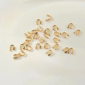 May include: A collection of gold-toned metal crimp beads, used for jewellery making. The beads are small and have a U-shape.