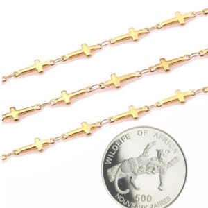 May include: Three gold chains with small cross charms. The chains are layered on top of each other. A silver coin with the words "Wildlife of Africa" and "500 Nouveaux Zaires" is in the bottom right corner of the image.