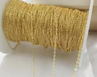 May include: A spool of gold-colored chain, with a length of chain hanging from the spool. The chain is a delicate, fine-link style.