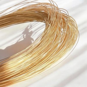 Puede incluir: Un carrete de alambre de color dorado, enrollado apretadamente. El alambre es delgado y brillante, y es perfecto para manualidades o la elaboración de joyas.