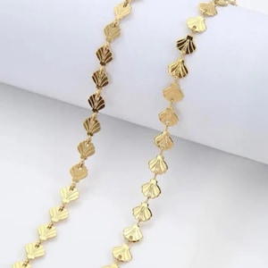 Peut inclure: Un collier en chaîne dorée avec un motif répétitif de petits pendentifs en forme de coquillage détaillés.
