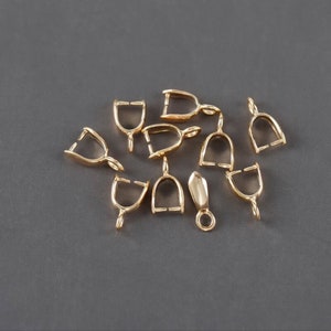 May include: A group of ten gold-toned metal pendant bails, with one additional gold-toned metal pendant bail with a pointed tip.