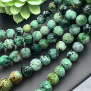 May include: A strand of green and black gemstone beads. The beads are round and have a mottled appearance.