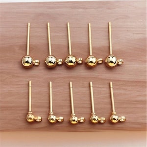 Peut inclure: Dix tiges de boucles d'oreilles dorées avec une petite boule à l'extrémité. Les tiges sont disposées en deux rangées de cinq.