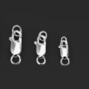 May include: Three silver-colored lobster claw clasps of varying sizes. Each clasp has a spring-loaded mechanism and a small ring at both ends. The clasps are displayed against a dark background.