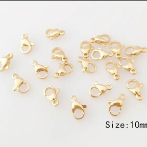 Puede incluir: Un grupo de 20 cierres de langosta de metal dorado, cada uno mide 10 mm. Los cierres están dispersos sobre una superficie blanca. Tamaño: 10 mm