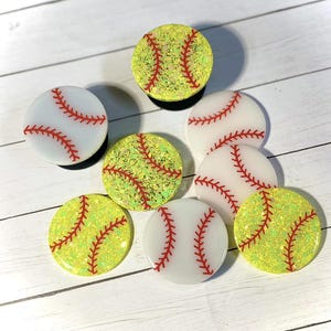 May include: Seven colorful phone grips with a softball design. The grips are made of white and yellow resin with red stitching.