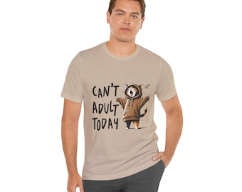 以下が含まれることがあります： 「CAN'T ADULT TODAY」の文字と、茶色のパーカーを着た漫画の猫が描かれたベージュ色のTシャツ。猫は腕を広げてあくびをしています。Tシャツは人が着ています。