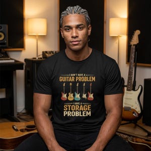 Puede incluir: Una camiseta negra de manga corta con un gráfico de cinco guitarras eléctricas de varios colores. El texto dice: I DON'T HAVE A GUITAR PROBLEM I HAVE A STORAGE PROBLEM. El diseño está centrado en el pecho con letras en amarillo y blanco.