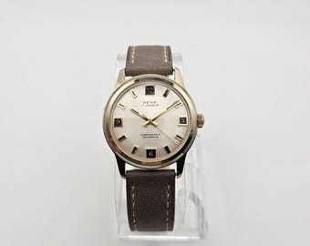 May include: A vintage wristwatch with a gold-toned case and a cream-coloured face. The watch features black numerals at the 3, 6, 9, and 12 o'clock positions, with gold-toned hands. The brown leather strap is stitched and secured with a buckle.