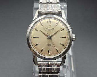 May include: A silver-tone Martinelli automatic wristwatch with a round champagne-colored dial, featuring the text Martinelli Automatic and 17 Jewels Incabloc. The watch has a textured silver metal link bracelet and a polished silver-tone case.