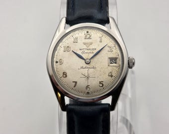 May include: A vintage Wittnauer Geneva automatic wristwatch with a silver-tone dial, black leather band, and date display. The watch face features Arabic numerals and blue hands. The watch is a classic timepiece.