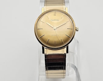 May include: A gold-toned wristwatch with a round face and a gold metal band. The watch face has black hands and black Roman numeral hour markers. The watch face also has the text "DUPONTE AUTOMATIC" printed on it.